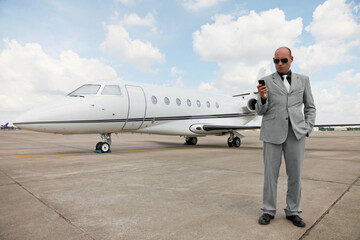 Man text messaging on the phone with private jet in the background