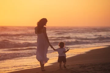 Tuinposter Strand zonsondergang A mom with her child walk on the beach of a beautiful shore at the sunset light
