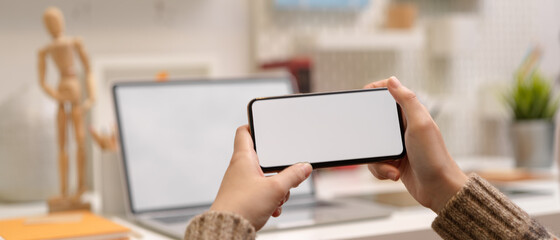 Female designer take a break and watching video on horizontal  mock-up smartphone while sitting at worktable