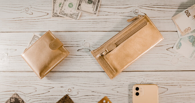 Two gold wallets, plastic cards, dollars, rubles, an expensive smartphone with two cameras on a wooden board background.