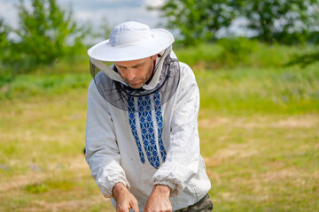 Naklejka na ściany i meble Beekeeper at apiary at the summer day. Man working in apiary. Apiculture. Beekeeping concept.