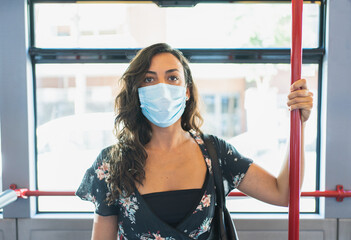 Young woman looking at camera with protective mask on face taken to the bus bar so as not to fall.