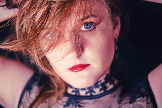 Redhead woman vampire with blowing hair, make-up for Halloween. Portrait of adult caucasian woman with white face on black background