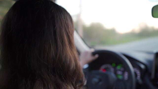 Beautiful brunette woman with long hair driving the car, rear view of woman drives automobile close-up.