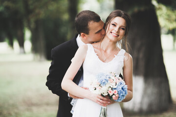 Stylish couple of happy newlyweds walking in the park on their wedding day with bouquet