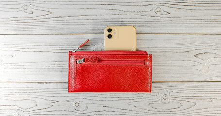 Red wallet with black clasp and an expensive yellow smartphone with two cameras on a wooden board background. Top view. Flatlay