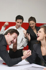 Businessman and businesswoman arm wrestling on table, the others cheering