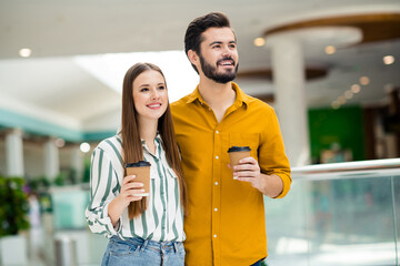 Portrait of positive cheerful dream couple man woman go walk shopping mall center enjoy weekend hold take-out cappuccino cup wear striped yellow shirt