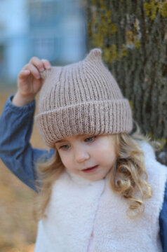 Picture of a smiling blonde toddler girl playing outside in the funny knitted hat with cat ears