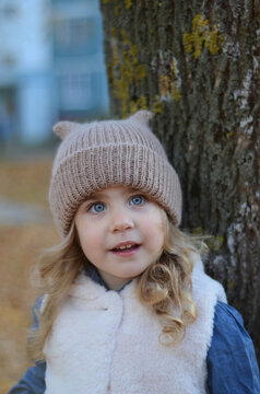Picture of a smiling blonde toddler girl playing outside in the funny knitted hat with cat ears