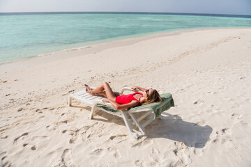 Full length profile photo of beautiful lady lying lounge chair azure blue water exotic resort empty desert beach sunbathing wear sun glasses red bodysuit enjoy sun rays ocean outside