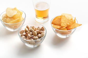 Appetizer in bar. Pistachio, chips and nachos in glass plates and glass of light beer