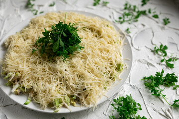 Layered salad with grated hard cheese with lettuce leaves and watercress greens on a white concrete background with texture