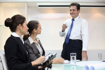 Businessman drinking coffee while talking to businesswomen in a meeting