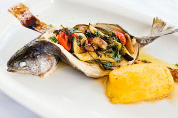 Baked trout on a plate. Delicious fish meal filled with vegetable ragout and served with potato puree. Studio shot.