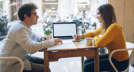 Successful startuppers discussing plan together for work smiling and gesturing, happy hipsters having friendly conversation about business information having meeting in coffee shop. mockup screen