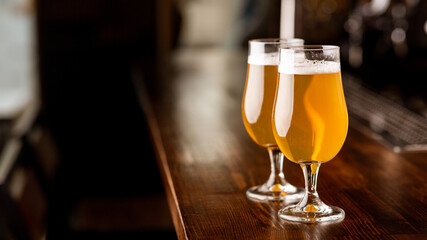 Service at pub. Glasses with beer in light on wooden bar counter