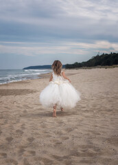 Fototapeta na wymiar Dance on the beach. A beautiful little girl in a white ballet dress walks and dances on a sandy beach.
