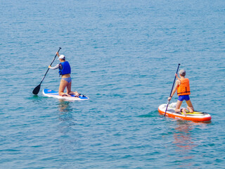 Two riders stand on the board and use the oars to wave, SUP-surfing on the background of sea blue water, the concept of an active lifestyle.