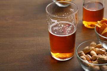 Client drink. Unfinished glass of beer and bottle, pistachio, chips in glass dishes on wooden table