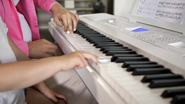 Private music teacher giving piano lessons to little girl. Hands close up.