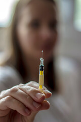 Women with injection in her hands. Young women is about to give injection to herself. Portrait of young woman holding syringe at home, selective focus. Close-up.