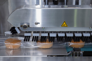 baked bread in food grade plastic bag on conveyor belt moves to seal in packing machine at...