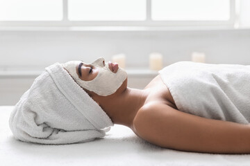 Black girl with white face mask resting on massage table