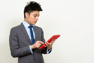 Portrait of young handsome Asian businessman in suit using digital tablet