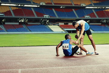 Male athlete laying on track, clasping leg in pain, another athlete helping