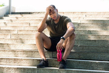 Tired black sportsman resting on stone stairs after workout outdoor