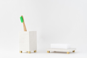 Eco natural wooden bamboo toothbrush in a holder and a soap in a soap dish. Minimal bathroom design, isolated. Natural light.