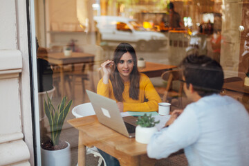 Teamwork. Two young startuppers sitting in cafe, talking and smiling with  computer screen and develop business plan. Business meeting in bar. share multimedia via wireless connection..