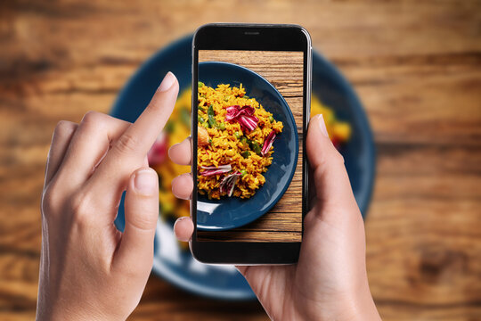 Blogger taking picture of delicious pilaf with chicken and vegetables at table, closeup. Food photography