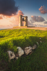Picturesque landscape with an ancient foggy bell in the center of the frame. Spring evening by the sea, magical sunset, ancient masonry, fresh grass and foggy bell. Copy space on the colorful sky. 