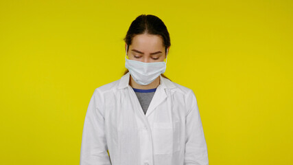 Young doctor in a protective medical mask and a white coat. Girl nurse on a yellow background. Coronavirus, flu