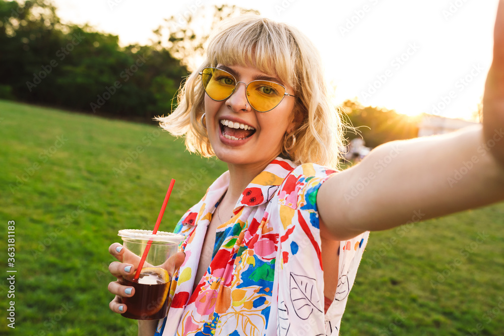 Poster image of happy young woman taking selfie photo and drinking soda