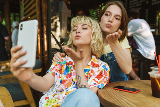 Image of women blowing air kiss and taking selfie on smartphone