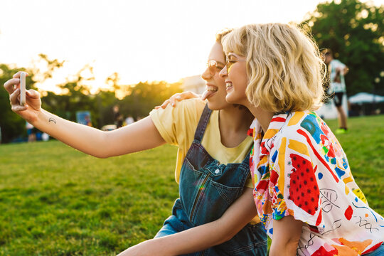 Image of amusing two women in sunglasses taking selfie on smartphone