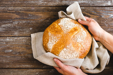 Hands holding a whole loaf of freshly baked bread with a golden crust. Homemade yeast-free pastries...