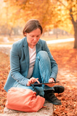 Woman using digital tablet on park bench in autumn