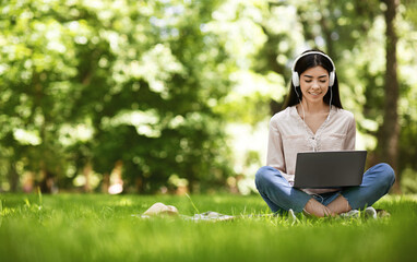 Joyful asian girl sitting on lawn with laptop, studying and listening music