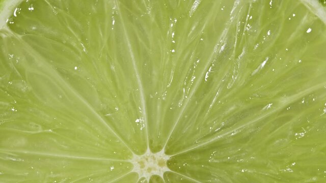 Macro view of lime slice rotation. Extreme closeup of green juicy texture of exotic fruit. Concept of healthy food, citrus products for cocktails. Colorful background.