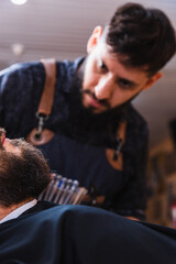 Barber focused on fixing his client's beard.  The focus is on the client's beard.