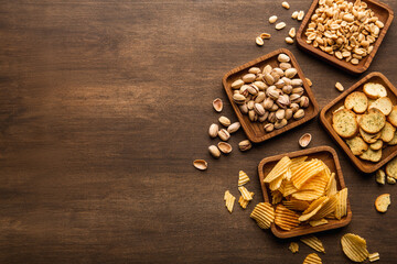 Delicious food to beer. Crackers, peanuts, pistachios and chips in square plates on brown wooden table