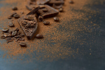 Dark chocolate stack, chips and cocoa powder with coffee beans on a dark background. Confectionery and food concept. Top view, copy space, selective focus..