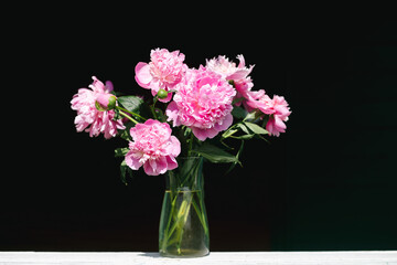 Pink peonies bouquet in vase on black background