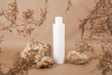 White blank cosmetic bottle with cream, moisturizing lotion or shampoo framed by dried plant...