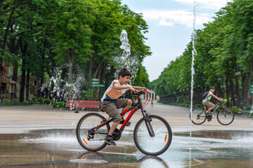 Children children have fun riding bicycles by the fountain on a hot summer day in a park.