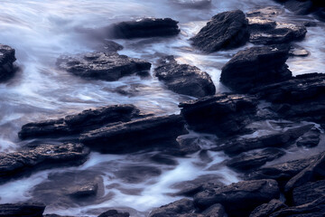Soft waves crashing into rocks on the shoreline
